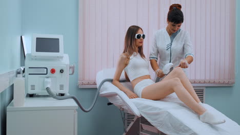 Young-woman-in-white-bathrobe-on-laser-hair-removal-procedure-in-beautician-clinic-slow-motion.-Doctor-removes-hair-from-legs-or-body-of-patient.-Concept